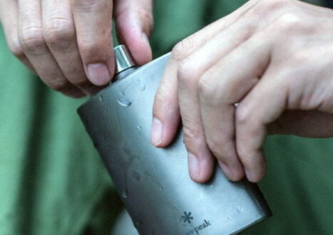 man holding titanium flask in wilderness