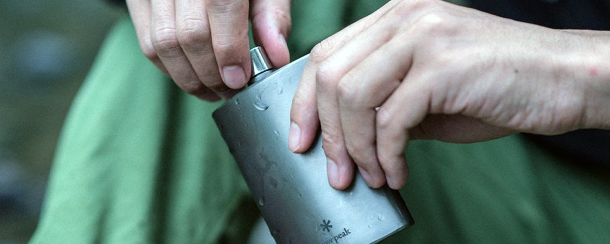 man holding titanium flask in wilderness